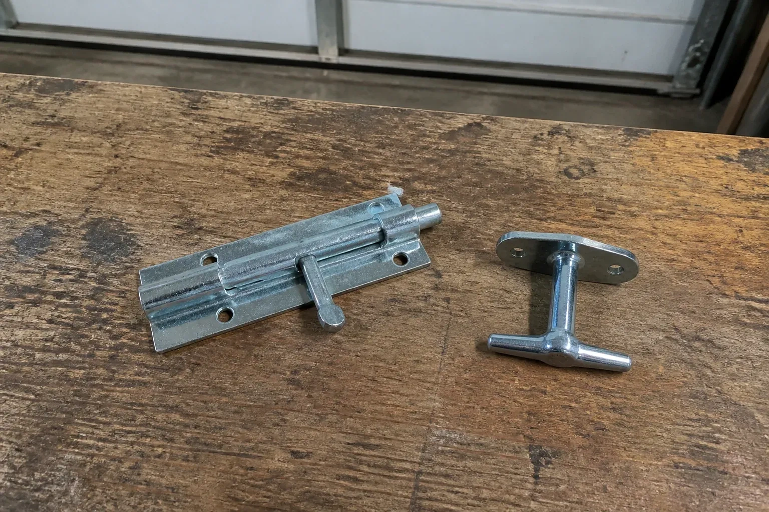 Detached slide bolt and T-handle on a wooden garage workbench. — Garage Door Manual Lock Repair, Toronto